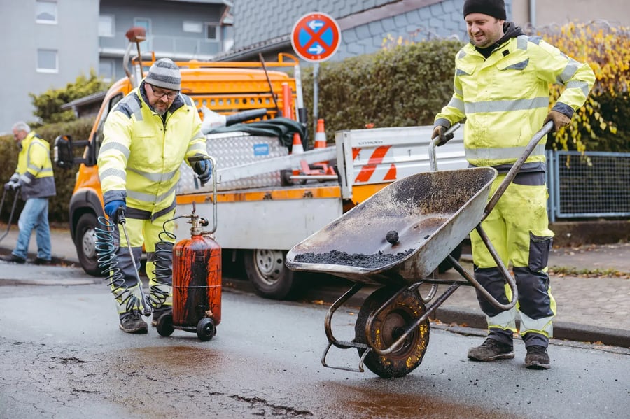 Straßenbauer mit Schubkarre reparieren die Straße und füllen ein Schlagloch