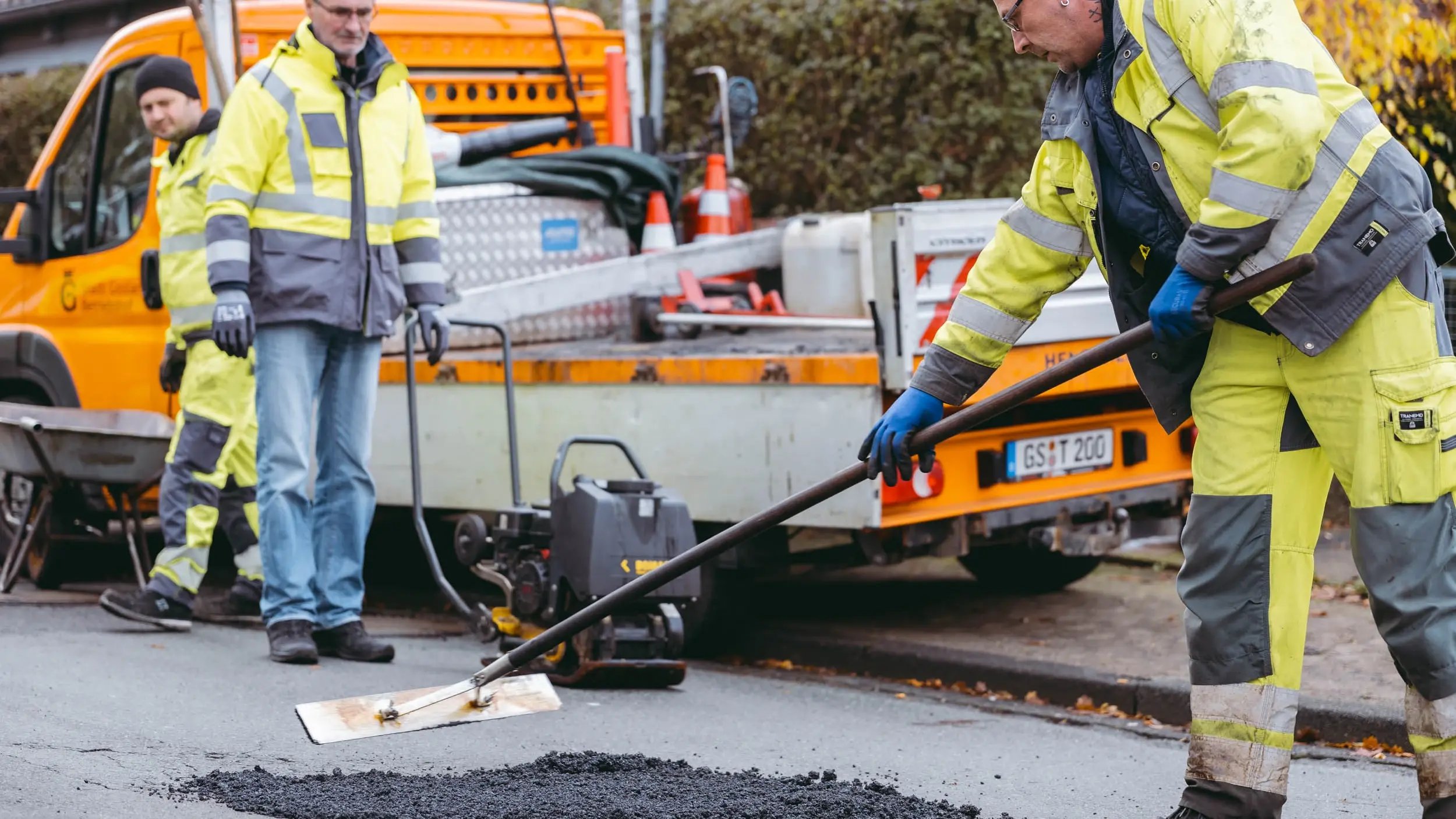 2 Bauarbeiter schließen ein Schlagloch mit Heißasphalt