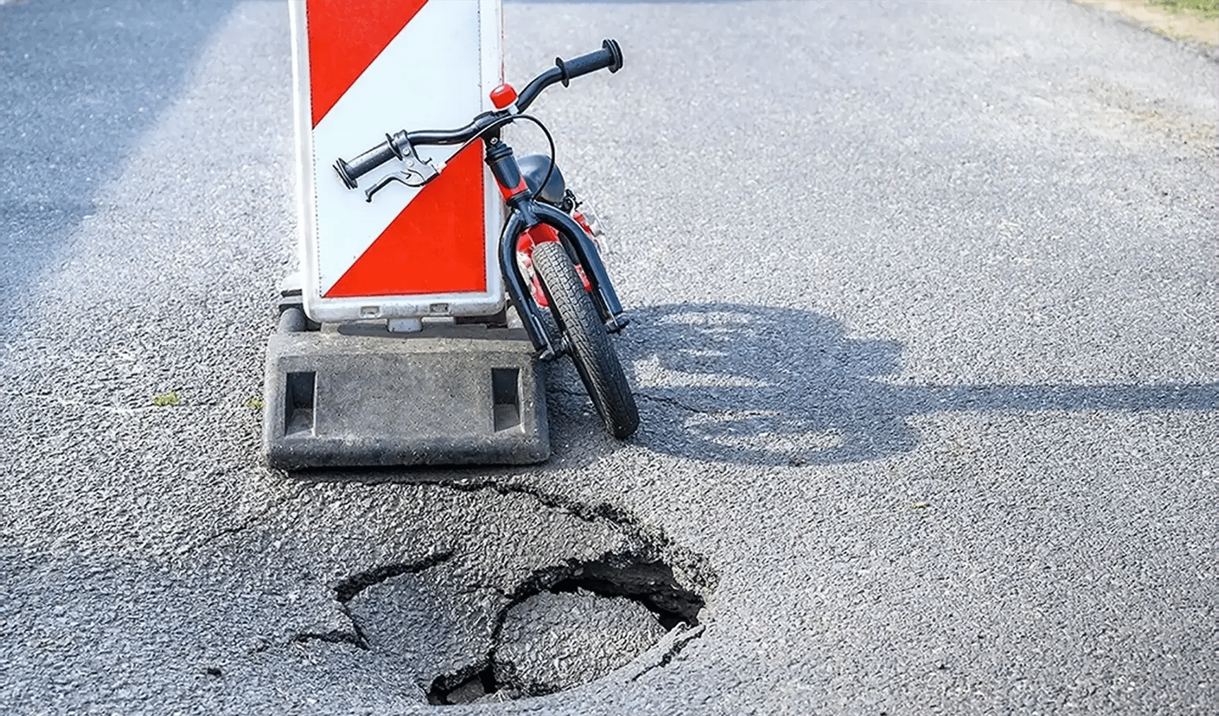 Fahrrad lehnt an einem rot-weiß gestreiften Schild vor einem Schlagloch