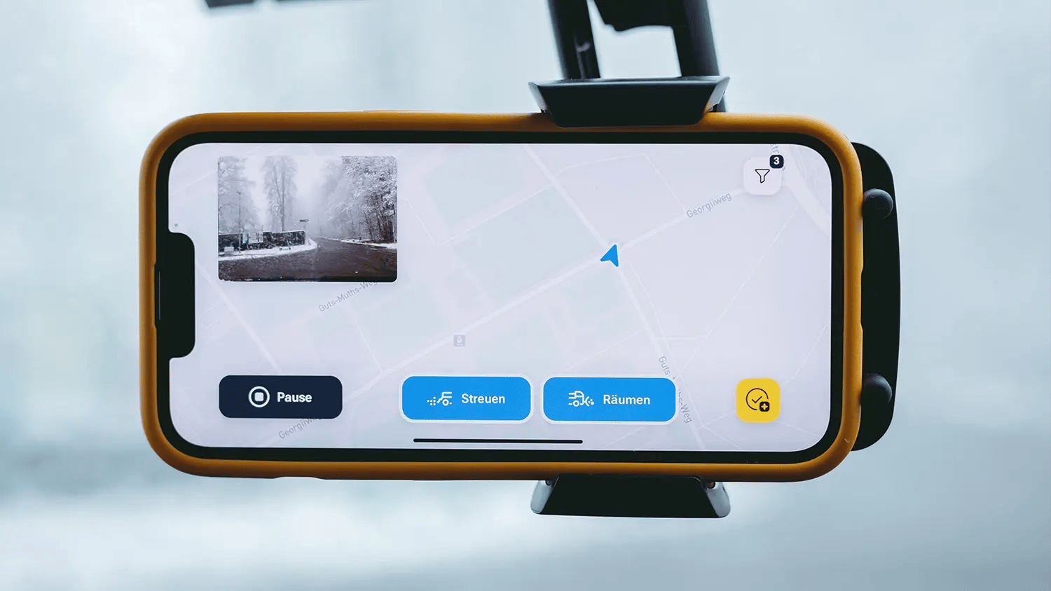 Smartphone in der Windschutzscheibe eines Fahrzeugs führt den Winterdienst mit der vialytics App durch